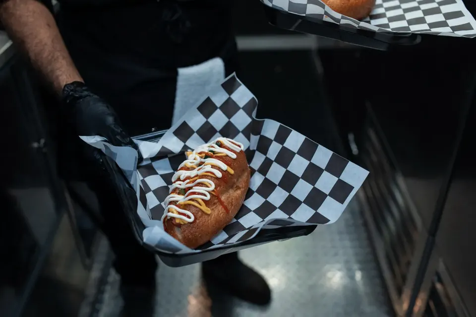 A hot dog with mustard and sauce served on checkered paper.