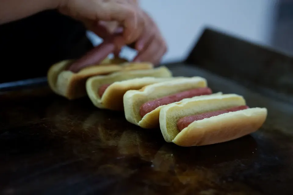 Hands placing hot dogs into buns on a griddle.